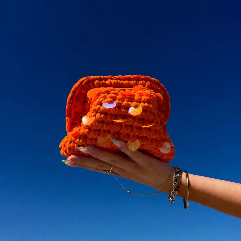 Mini clutch Ibiza orange avec des sequins oranges, tenu par une main avec le ciel bleu en arrière plan