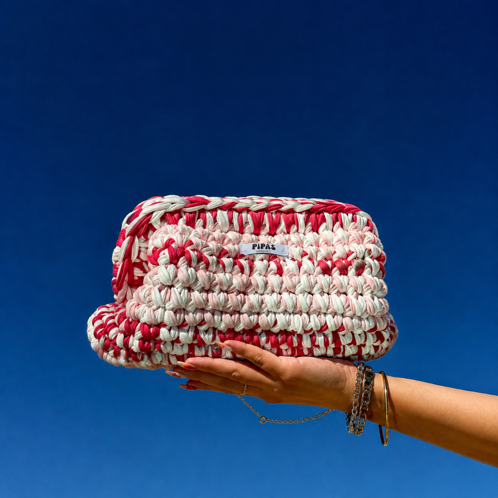 Clutch Amor rose et blanc, tenu par une main avec le ciel bleu en arrière plan