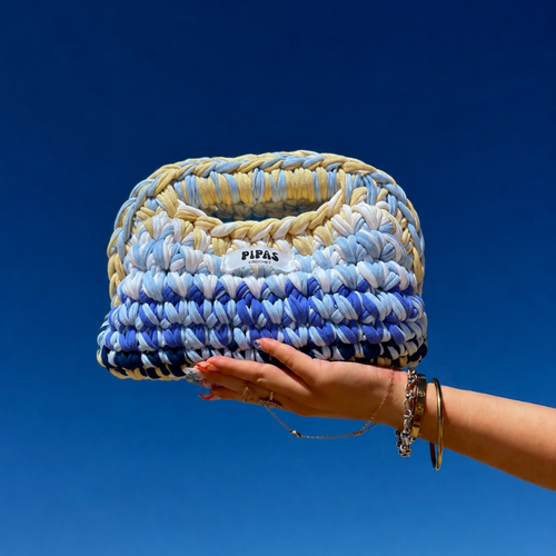 Clutch Capri bleu, jaune et blanc tenu par une main avec le ciel bleu en arrière plan