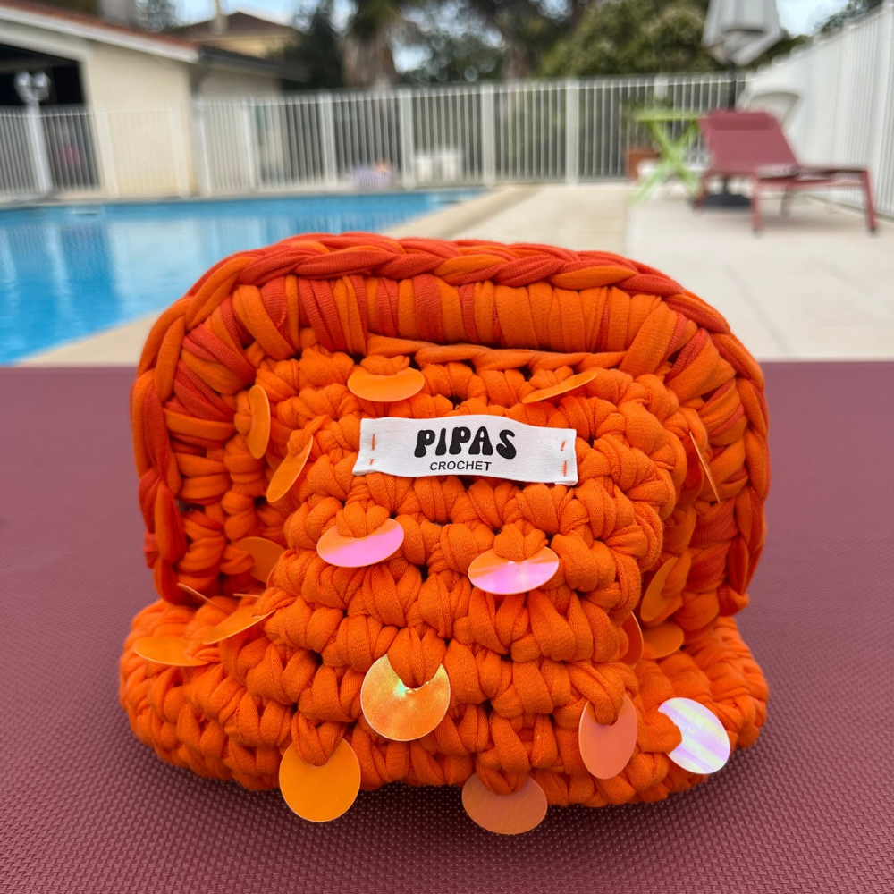Mini Clutch Ibiza orange avec sequins oranges posé sur un transat