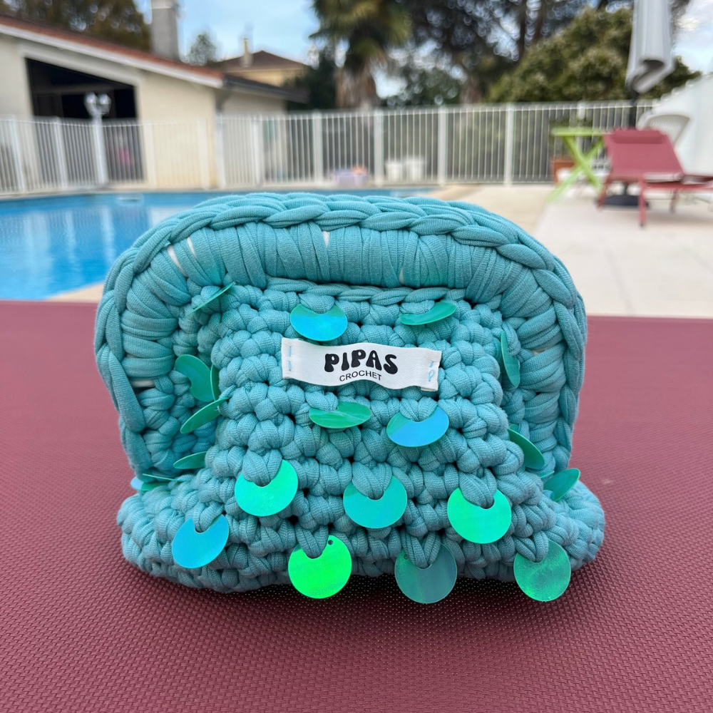 Mini Clutch Palma turquoise avec sequins turquoises posé sur un transat