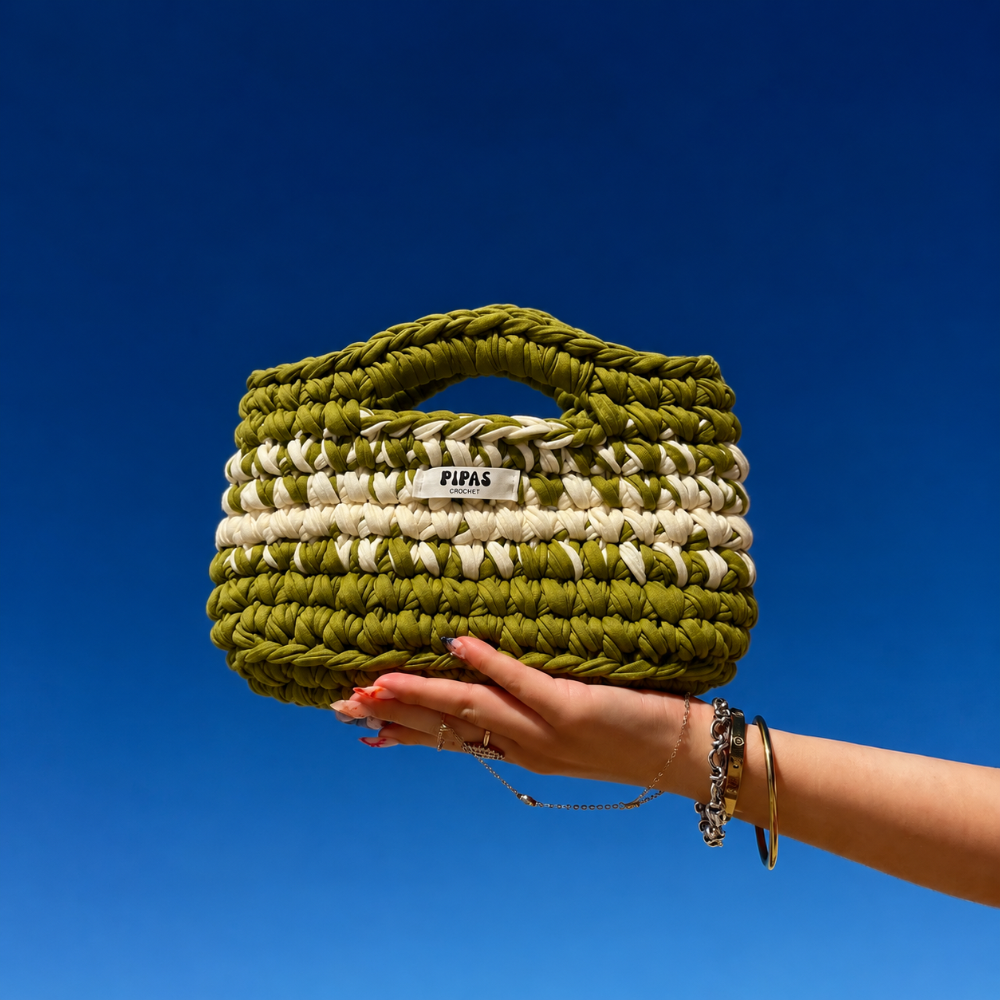 Sac Bali, vert et crème, tenu par une main avec le ciel bleu en arrière plan