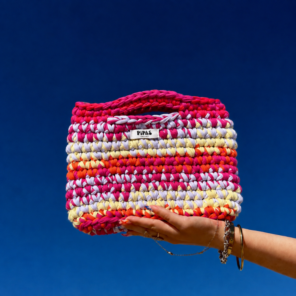 Sac Marrakech rose, rouge, lilas et jaune, tenu par une main avec le ciel bleu en arrière plan