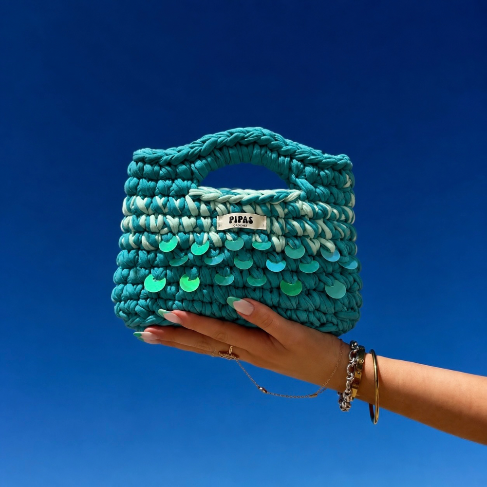 Sac Palma turquoise avec des sequins turquoises, tenu par une main avec le ciel bleu en arrière plan